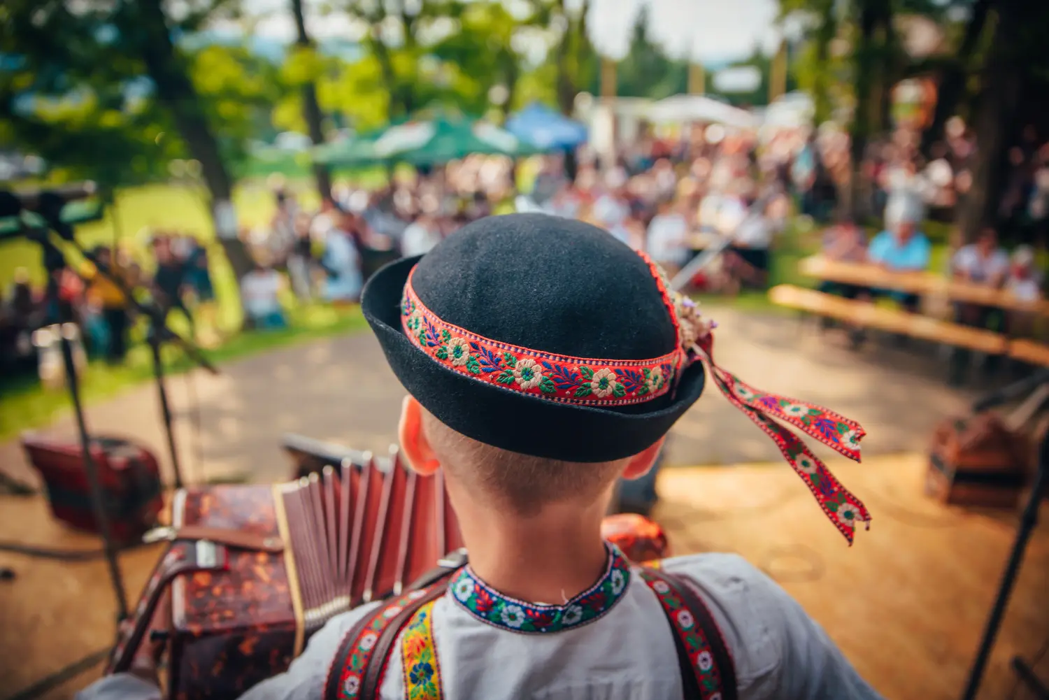 Junger Mann mit Akkordeon in slowakischer Tracht und Folklorehut. Vor der Menge